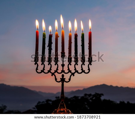 Close-up of burning candles on menorah are traditional symbols of Hanukkah Holiday of Light, selective focus on candles, blurred background of mountains and morning sky