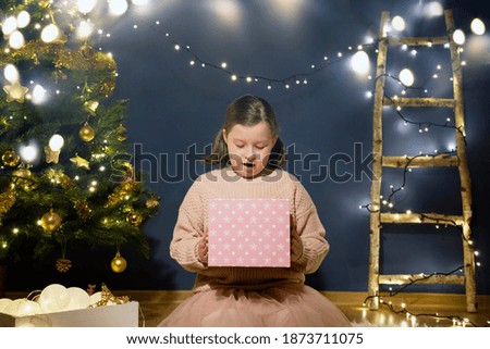 Cheerful cute child girls opening gift box near the Christmas tree.