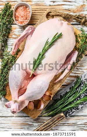 Raw whole farm goose on butcher cutting board. White wooden background. Top view