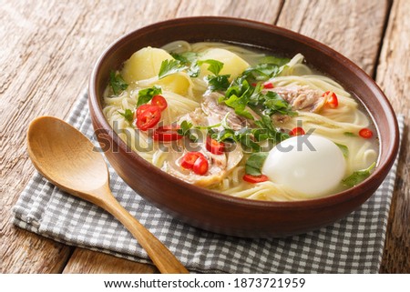Peruvian food Caldo de Gallina chicken noodle soup with boiled egg and herbs close-up in a plate on the table. horizontal
