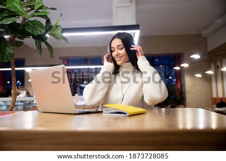Happy positive young Asian businesswoman wears headphones, listens to her favorite energetic audio music, relaxes in the office, smiles at the employee, enjoying a fun educational online lecture.