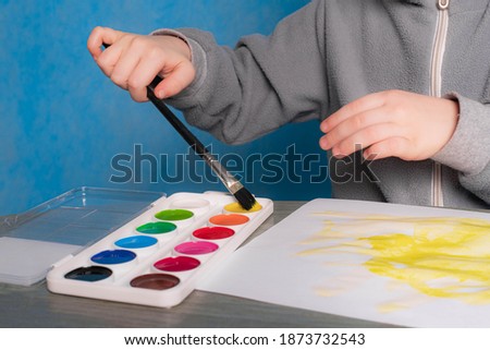 The boy paints a monochrome background. Advertising paints with a child. A boy with paints on a plain background . Happy childhood. Hobby drawing. Children's drawing. Paints for children. Classes at