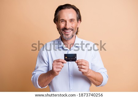 Photo of cheerful bearded man demonstrate debit card toothy smile wear shirt isolated beige color background