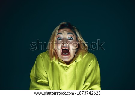 Screaming. Portrait of young crazy scared and shocked caucasian woman isolated on dark background. Copyspace for ad. Bright facial expression, human emotions concept. Looking horror on TV, cinema. Royalty-Free Stock Photo #1873742623