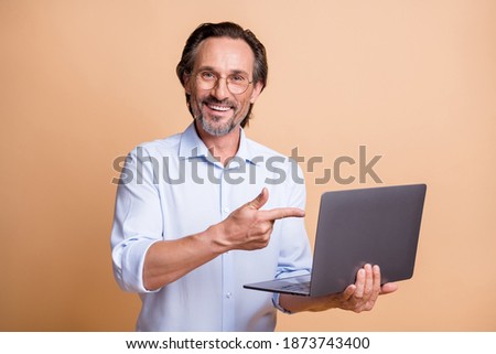 Photo of freelance promoter guy hold pc indicate finger gadget wear glasses shirt isolated beige color background