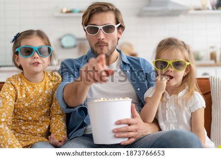 Happy family watching TV at home and eating popcorn.