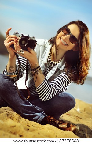 Happy laughing girl with camera on the beach sitting on the sand