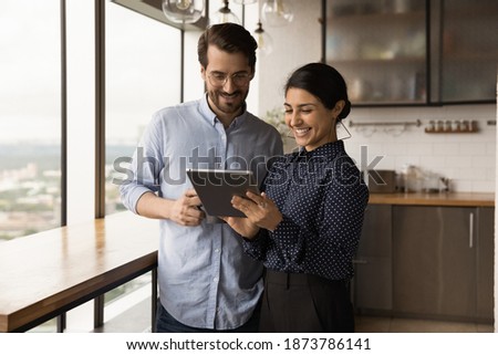 Smiling multiracial young colleagues look at tablet screen discuss financial business online project on gadget. Happy diverse multiethnic coworkers cooperate use pad device at work break in office. Royalty-Free Stock Photo #1873786141