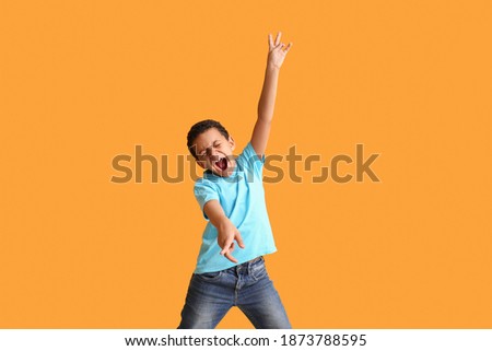 Little African-American boy dancing and singing against color background