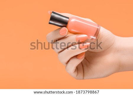 Female hand with orange nail design. Orange nail polish manicure. Woman hand hold orange varnish on orange background