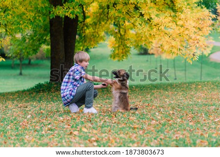 Boy hugging a dog and plyaing with in the fall, city park