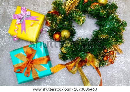 a wreath of Christmas tree branches with Christmas decorations and gifts next to it on a gray background top view