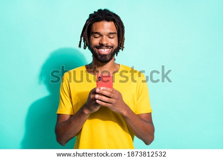 Photo portrait of afro american guy holding phone in two hands isolated on vivid teal colored background