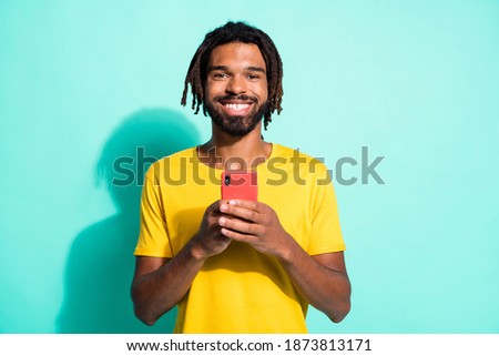 Photo portrait of smiling afro american guy holding phone in two hands isolated on vivid cyan colored background