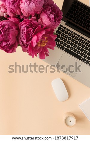 Home office desk workspace with laptop, pink peony flowers bouquet on peach background. Flat lay, top view blog, website, social media concept.