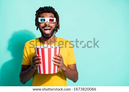 Photo of young happy smiling excited crazy afro man in 3-D glasses hold box of pop corn isolated on turquoise color background