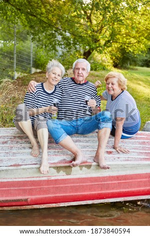 Happy seniors group as friends drinking red wine by the lake in summer