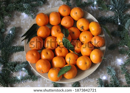 Lots of tangerines laid out on a plate and decorated with garlands and fir branches