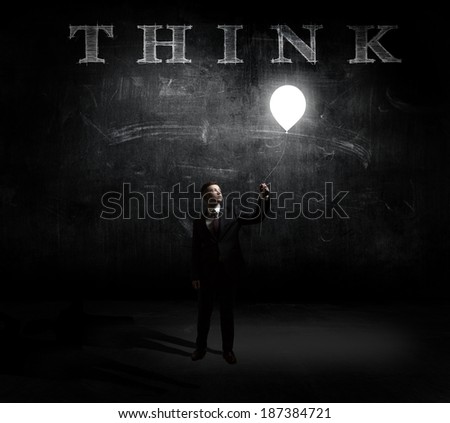 Young man holding a light at his hands against dark background with a word think