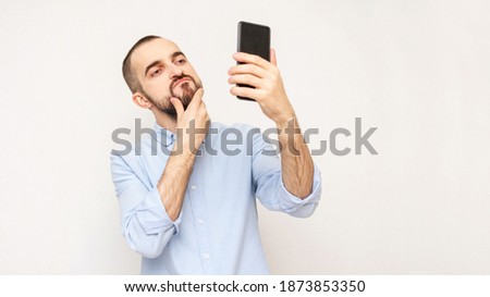 Narcissistic bearded takes a selfie with smartphone, white background, copy space, 16:9 Royalty-Free Stock Photo #1873853350