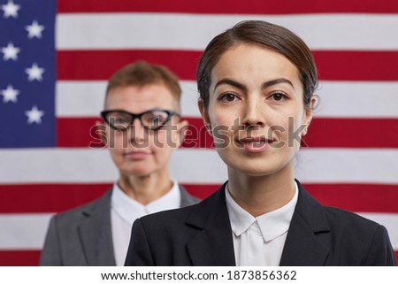 Close up portrait of young female politician looking at camera and smiling while standing against USA flag background, copy space
