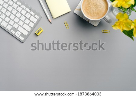 Flat lay, top view office table desk. Workspace with cup of coffee, keyboard, yellow office supplies and flower on grey background. Minimal style freelancer workplace.