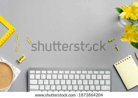Flat lay top view office desk table. Workspace with computer keyboard, coffee cup, yellow stationery and flower on grey background. Freelancer workplace in minimal style.