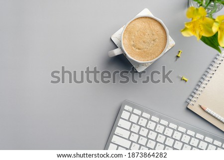 Flat lay top view home office desk. Modern workspace with cup of coffee, yellow office supplies, flower, keyboard on grey background. Minimal style.