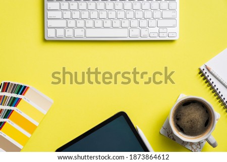 Professional creative graphic designer desk with computer keyboard, tablet, color palette, cup of coffee, notebook on yellow background. Flat lay, top view. 