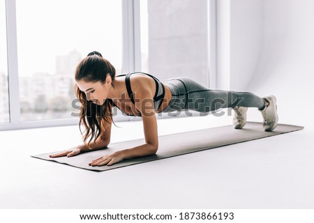 Slim fitnes young girl with ponytail doing planking exercise indoors at home gymnastics. Royalty-Free Stock Photo #1873866193