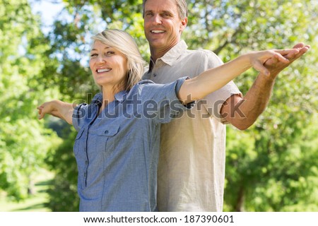 Portrait of happy couple standing arms outstretched in park