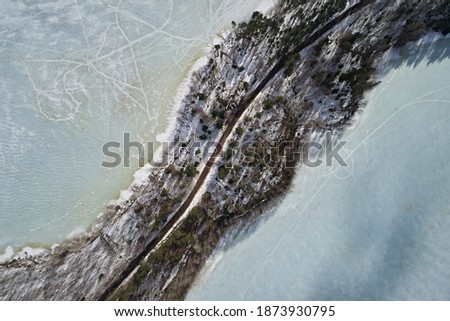 Aerial view of the road and forests separating the two shores of the lake in winter. Beautiful abstract landscape of northern nature with drone.