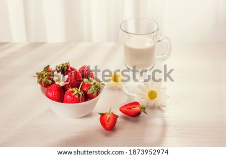 to cut strawberries, a glass of milk, chamomiles on a white wooden surface in the early morning