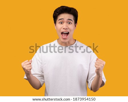 Yes, Achievement Concept. Excited young asian man cheering and screaming, celebrating victory. Emotional overwhelmed guy yelling and shaking clenched fists, isolated over orange background