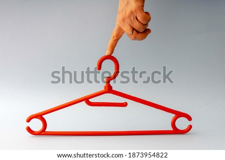 Woman hand holding red hanger with one finger, isolated on blue background. 