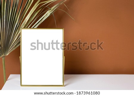Gold frame copyspace and plant on white table with dark orange wall background