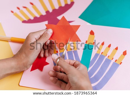 a girl makes a card for happy Hanukkah with her hands, a candelabra and candles on the card