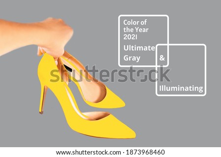 Bright illuminating yellow high heel shoes in woman's hand on gray color background. Concept of Color of the Year 2021. Fashion outfit abstract art layout. Front view. Valentine's day concept.