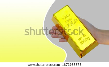 Human hand holding the gold bar on yellow and gray background