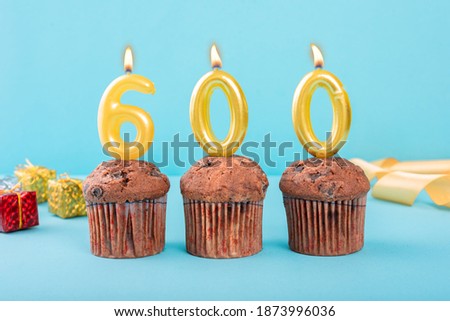 600 Number gold candle on a cupcake against a pastel blue background six hundred year celebration