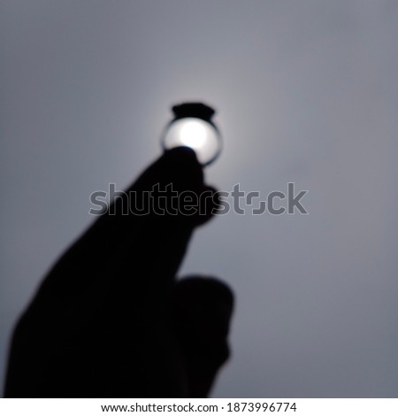 Blurr image of hand's silhoutte. finger and Ring Symbol, in black color againt the blue sky. The sunrise have a tendered shine, put on the ring. make an exotic and amazing captured. 