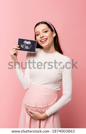 happy young pretty pregnant woman holding ultrasound scan isolated on pink