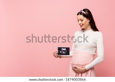 happy young pretty pregnant woman holding ultrasound scan isolated on pink
