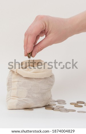 in a small bag, standing on a white background, the hand folds coins. Vertical photo, close-up. Russian money. The idea is enrichment, increasing profits.