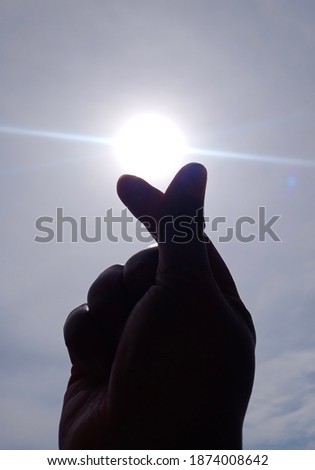 Blurr image of the sunrise through the fingers. LOVE Symbol. againt the blue sky. The sunrise have a bright shine, put on between two fingers. make an exotic and amazing captured. 