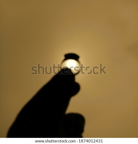 Blurr image of sunrise through the silhouette of ring and hand which in the black color. The sunrise have a bright shine, put on between two fingers. make an exotic and amazing captured. in warm tone
