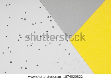 Paper background with metallic shiny stars and glitter in two trendy colors - yellow and gray. Demonstrating colors of 2021 year. Festive backdrop for your design.
