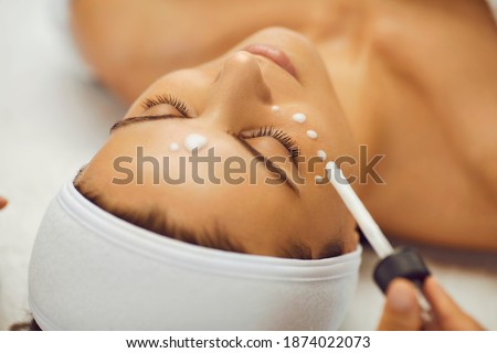 Close up of relaxed beautiful woman with closed eyes receiving facial rejuvenation procedure with moisturizing serum in beautician's office. Concept of facial skin care. Royalty-Free Stock Photo #1874022073
