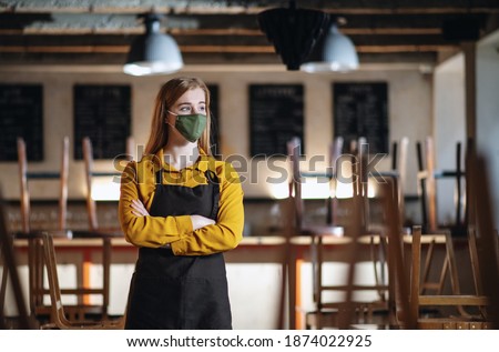 Frustrated waiter standing in closed cafe, small business lockdown due to coronavirus. Royalty-Free Stock Photo #1874022925