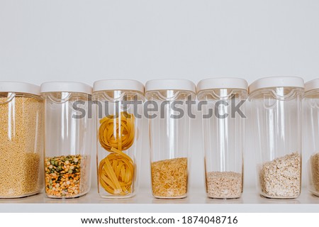 Stocked kitchen pantry with food - pasta, millet, oat flakes, peas, buckwheat, lentils, rice and sugar. The organization and storage in a kitchen in plastic containers. White modern kitchen
